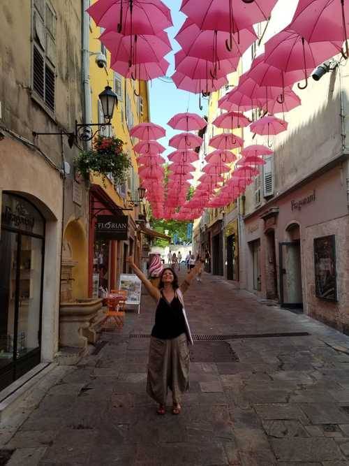 Melanie Benezet (French alumni) standing in a street under hundreds of open red umbrellas